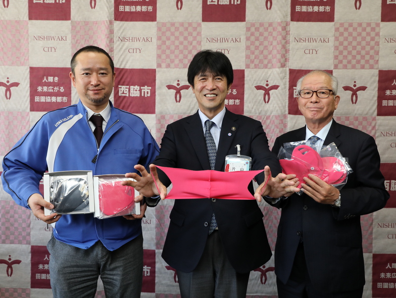 寄付されたマスクを手に持つユタックス宇高社長と、片山市長、笹倉教育長