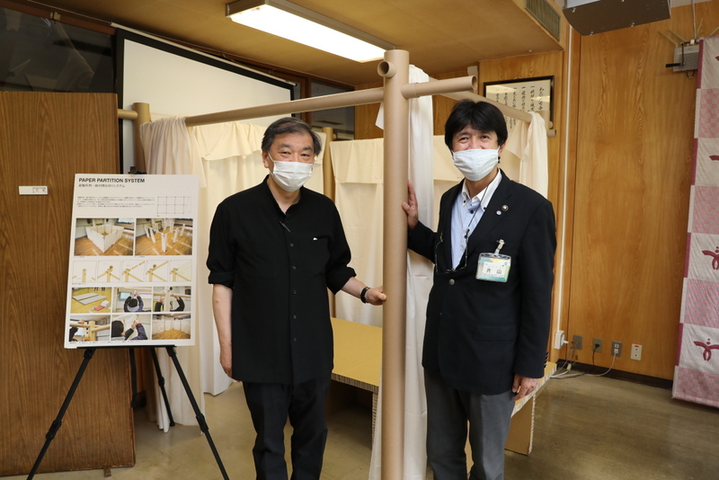 間仕切りシステムと紙製ベッドの前にて